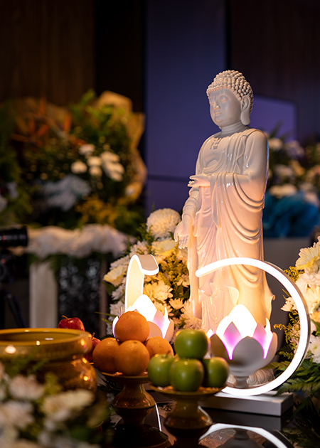 A serene figure of Buddha at the altar, accompanied by lotus lamps and fruits